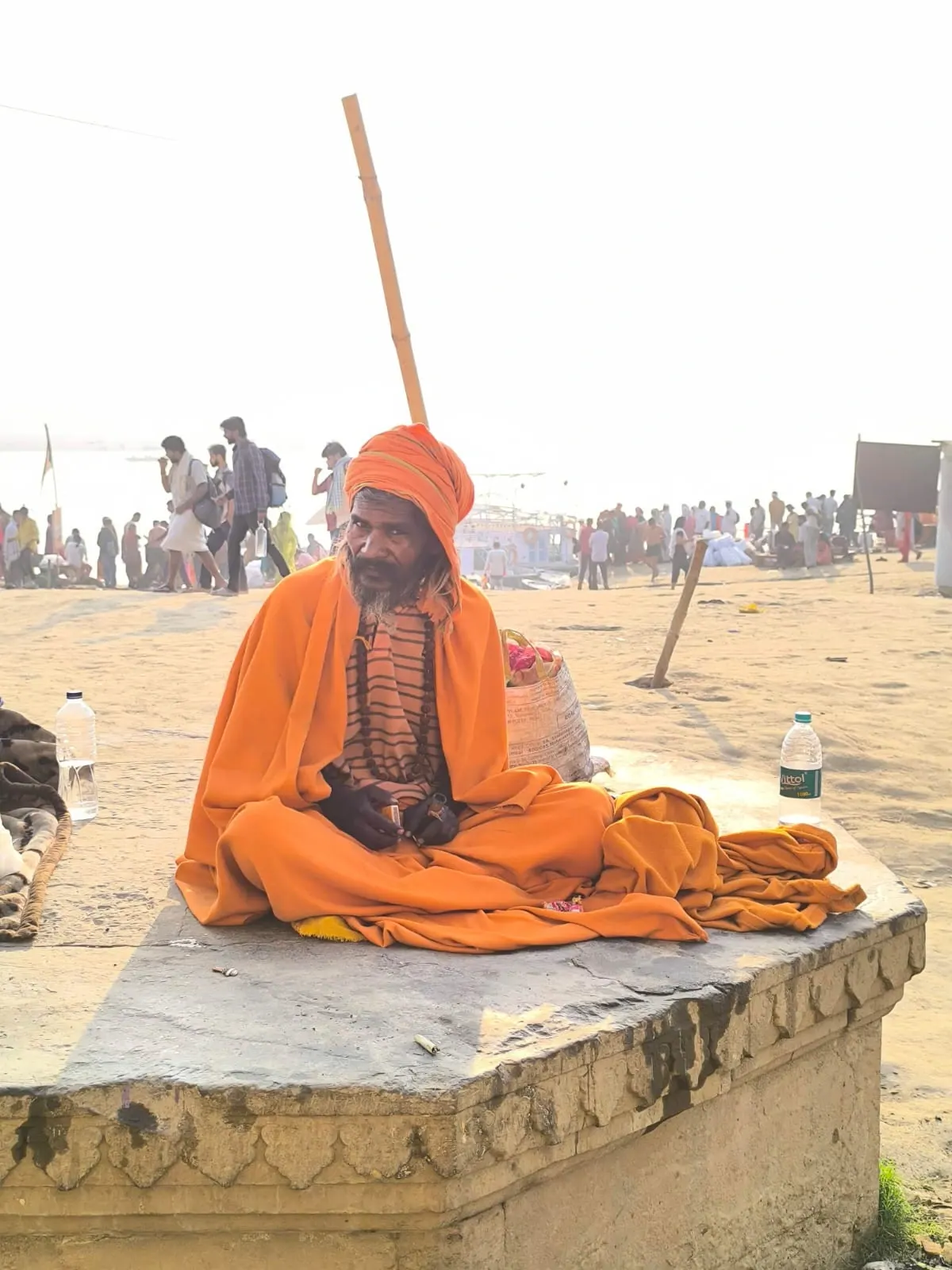Un sadhu in abiti arancioni seduto in meditazione su un muretto, con un lungo bastone