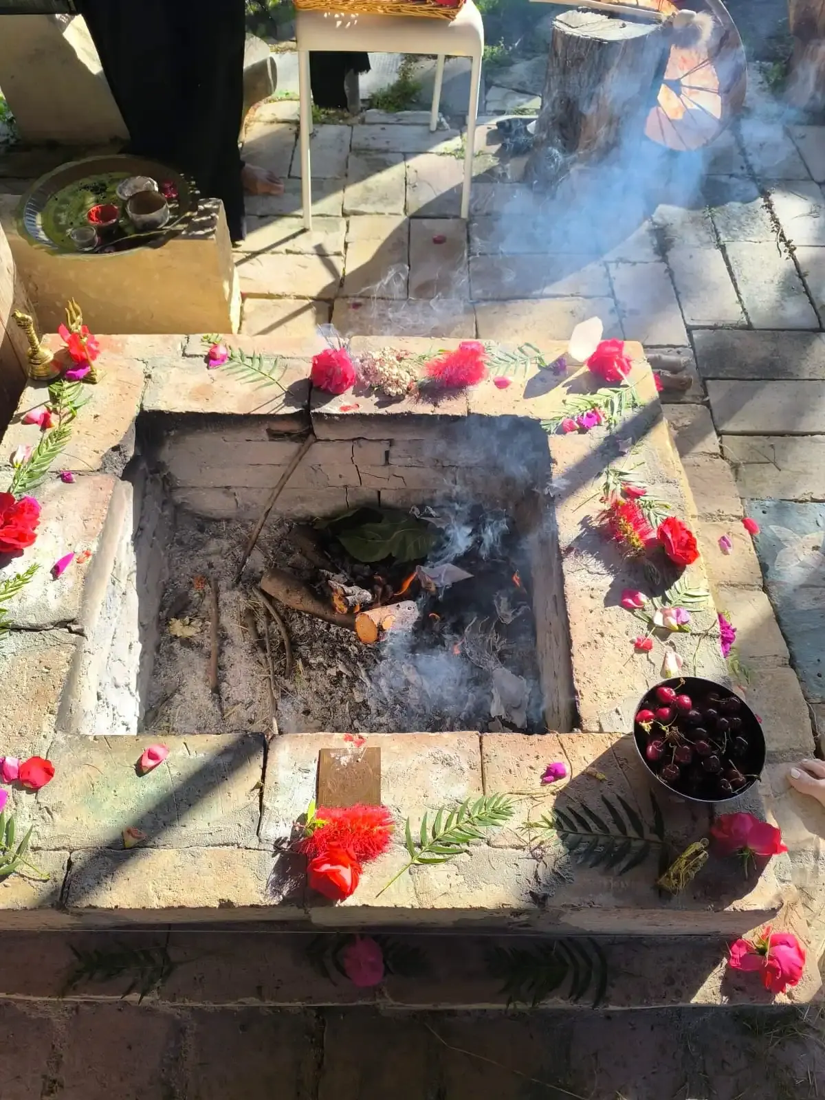 Un braciere rituale di pietra ancora fumante, circondato di rose rosse e offerte