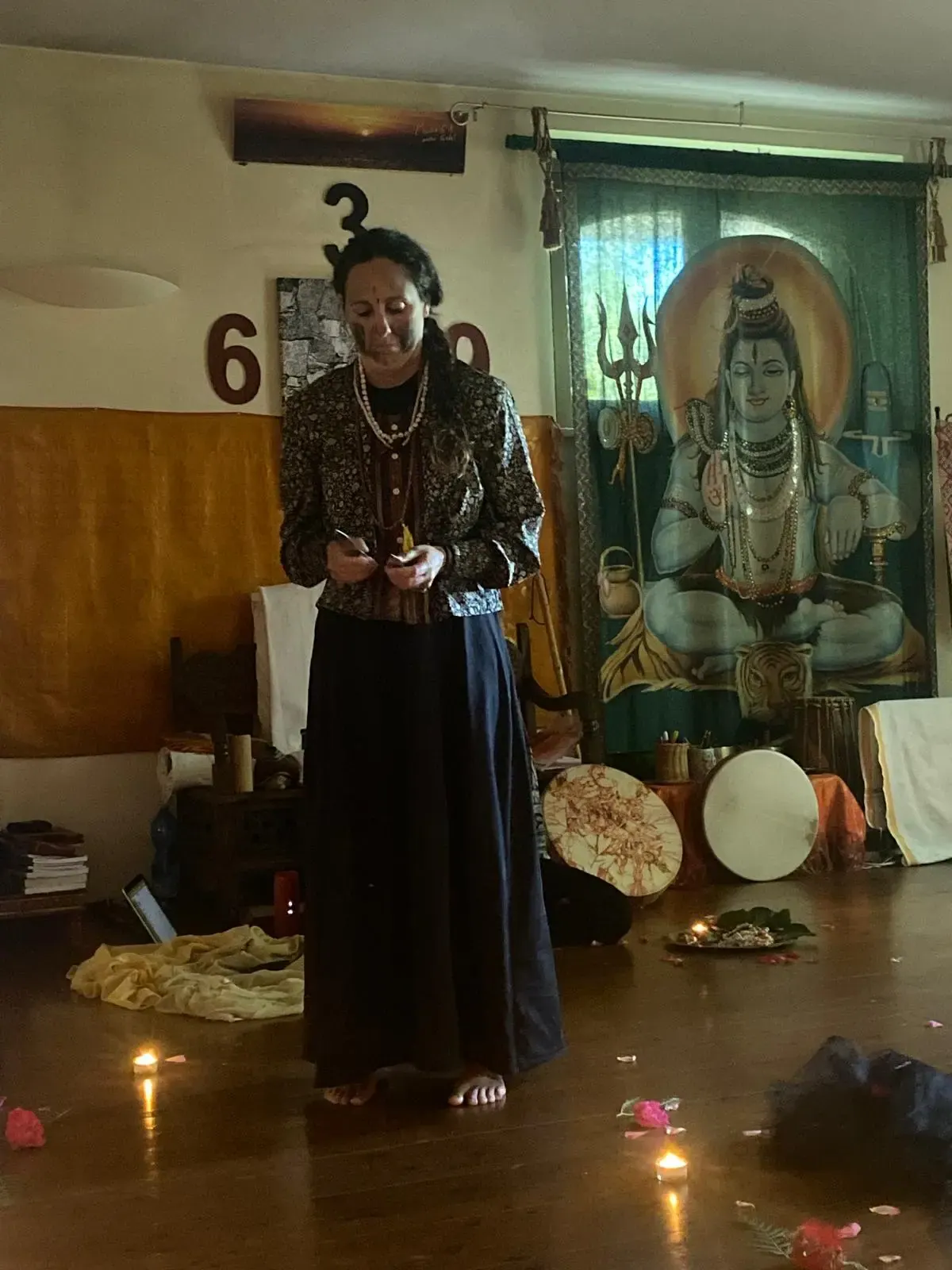Una donna in piedi nella sala del cerchio, fra candele accese e un dipinto di Shiva