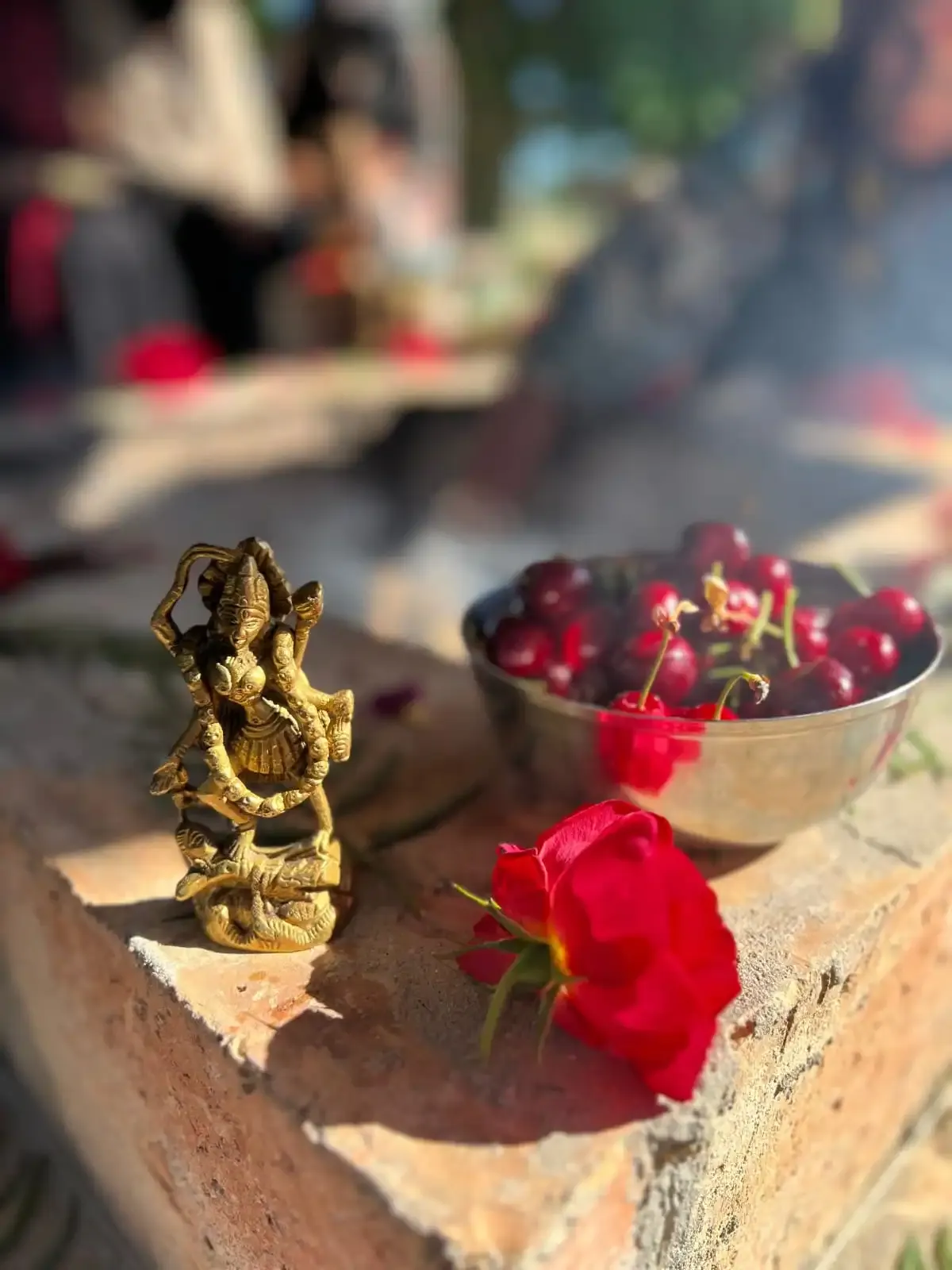 Una statuina dorata di Ganesha accanto a una ciotola di ciliegie e a una rosa rossa