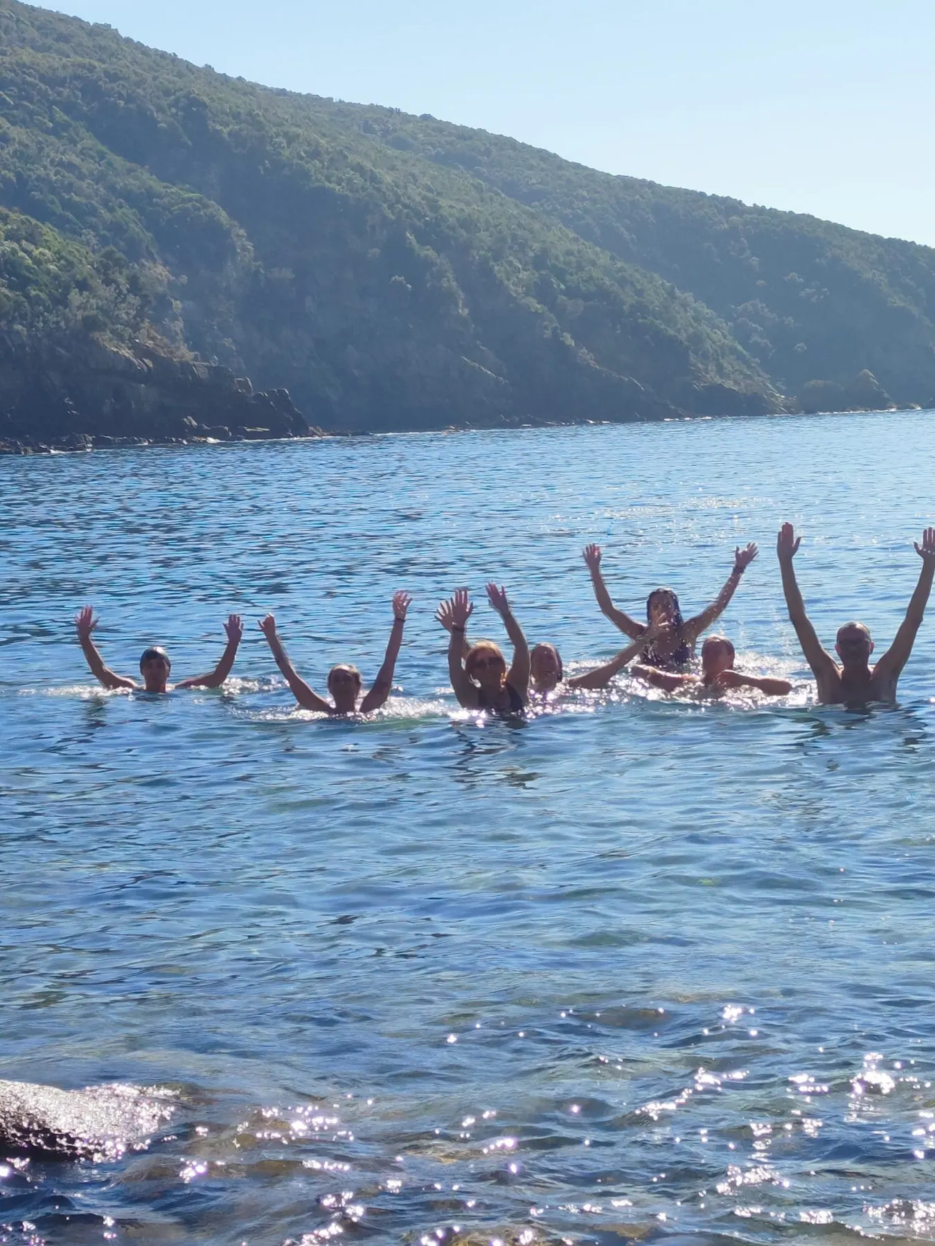 Le partecipanti in acqua nel mare di Baratti, con le braccia alzate verso il cielo, davanti alla collina verde