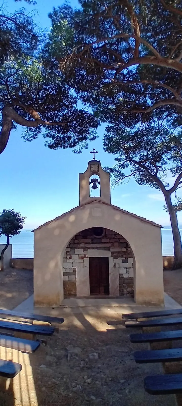 La piccola chiesa di San Cerbone a Baratti, in pietra, fra i rami dei pini e il cielo azzurro