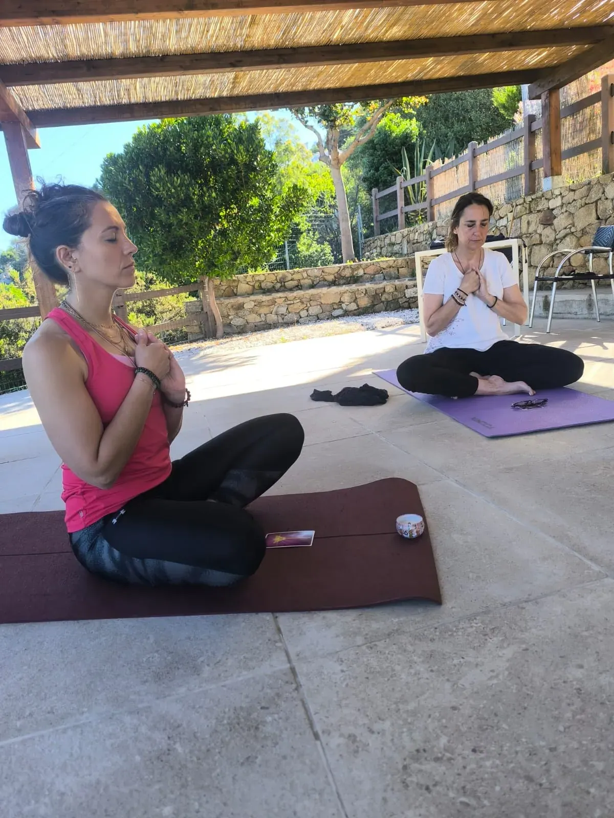 Due allieve in meditazione a gambe incrociate sui tappetini, a mani giunte