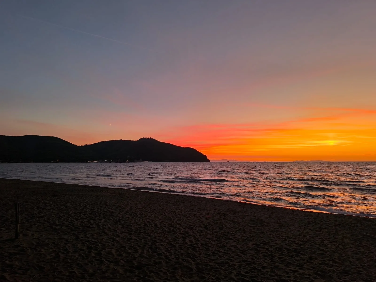 Il tramonto sul golfo di Baratti visto dalla spiaggia, con il promontorio di Populonia in controluce